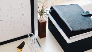 Calendar, tape, plant, and notebooks placed on a desk
