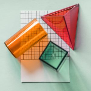 A piece of graph paper with a red pyramid, an orange cylinder, and a green cube on top.