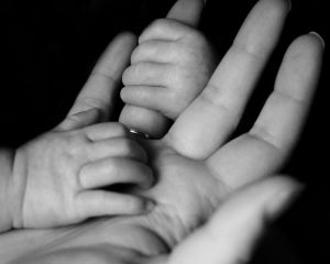Infant hands grasping an adult hand with a ring on it.