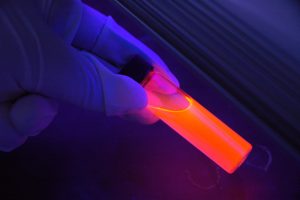 Gloved hand holding a glowing orange vial in lowlight.
