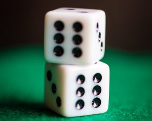 Two dice showing sixes, stacked on green felt with a dramatic shadow background.